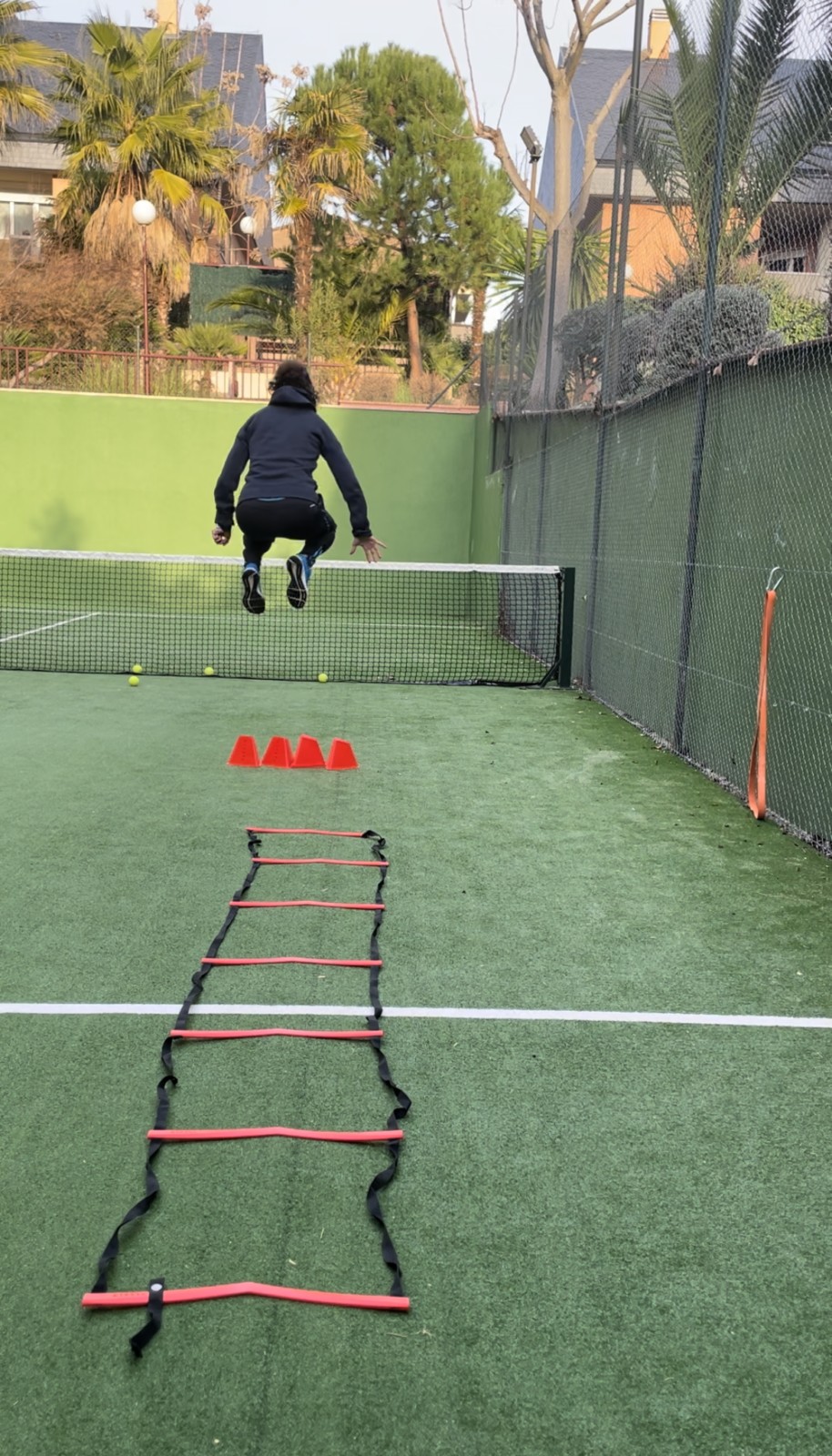 Ejercicio pliométrico con escalera de coordinación y conos en pista deportiva